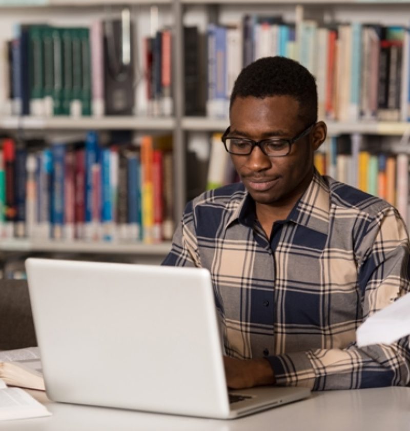 In The Library - Handsome African Male Student With Laptop And Books Working In A High School - University Library - Shallow Depth Of Field ID:91719221
