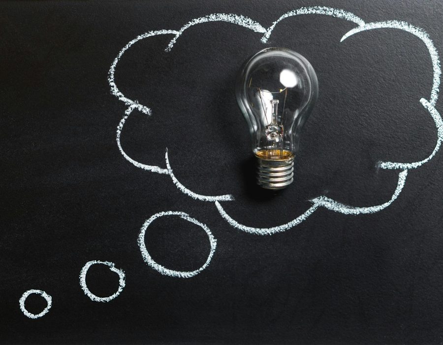 Light bulb laying on chalkboard with drawn thought bubble, symbolizing creative ideas.
